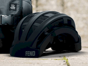 Fend helmet in black folded shown outside next to a backpack